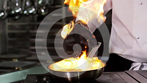 Close-up of a professional chef in black gloves in the kitchen of a restaurant cooks in the style of Flambe.Fruits and