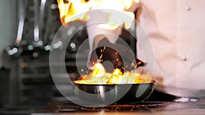 Close-up of a professional chef in black gloves in the kitchen of a restaurant cooks in the style of Flambe.Fruits and