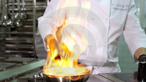 A close-up of a professional chef in black gloves in the kitchen of a restaurant cooks in the style of Flambe. Fruits