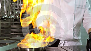 A close-up of a professional chef in black gloves in the kitchen of a restaurant cooks in the style of Flambe. Fruits