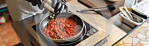 Close up of professional chef in uniform adds spices into pan with dish in restaurant kitchen