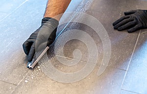Close up of professional cleaner cleaning grout with a brush blade and foamy soap on a gray tiled bathroom floor photo