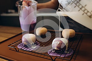 Close up of professional confectioner hands spooning the warm chocolate glaze unevenly over the profiteroles for