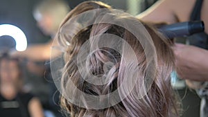 Close-up. Professional hairdresser using curling iron. Hair curls in salon,