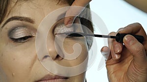 Close-up of professional make-up artist applying eyeliner on eyelid. Stylist is doing make up for female by eyeliner