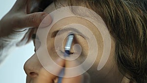 Close-up of professional make-up artist applying eyeliner on eyelid. Stylist is doing make up for female by eyeliner