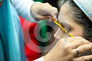 Close up of professional make up artist hand applying eyelash extension cosmetic to young Asian female model face with tool