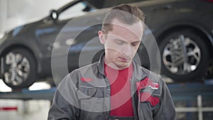 Close-up of professional male maintenance engineer standing in repair shop and using tablet. Caucasian auto mechanic