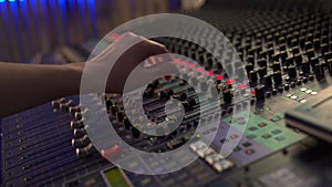 Close-up. Professional mixing console in the studio, female hand controls the sound, with LED backlight