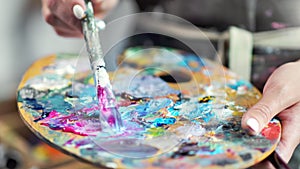 Close-up professional painter hands mixing color paint on palette creating amazing picture