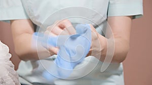 Close-up Professional woman beautician puts on her hands blue rubber clean sterile gloves before doing the procedure for