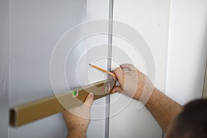 Close-up of professional worker using level for wall and pencil