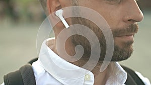 Close-up. Profile of a bearded middle-aged man with white wireless headphones in his ears.