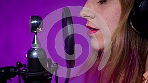 close-up profile of female wearing closed headphones singing into a microphone