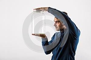 Close up profile portrait of a curious businessman holding an empty glass jar in his hands isolated over white background