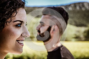 Close up of a profile view of a smiling blue eyes woman`s face in the foreground and a smiling beard man`s face in profile in th