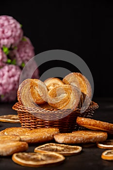 Close up of puff pastry in basket with lilac flowers, selective focus, on wooden table, black background