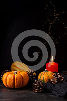 Close-up of pumpkins for halloween and burning orange candle, selective focus, on dark wooden table, black background and lights