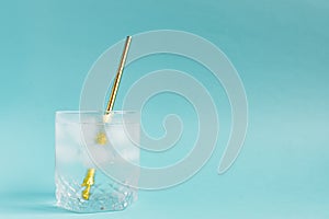 Close up of pure water with ice and paper straw in transparent glass and sun glare on blue  background