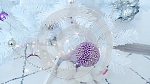 Close-up of a purple Christmas ball hanging on a white Christmas tree