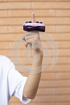 Close-up of a purple doughnut with blueberries on the finger of an American man wearing a white T-shirt