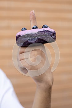 Close-up of a purple doughnut with glazed blueberries on the finger of a afro man wearing a white T-shirt