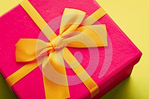 Close-up of a purple gift box with a yellow ribbon tied with a bow on a yellow background