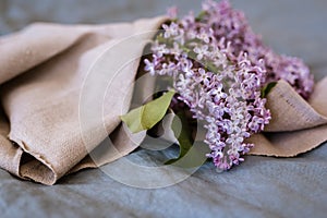 Close-up of purple lilac flowers branch in bloom on blue linen sheet with neutral linen towel, eco lifestyle concept, still life,