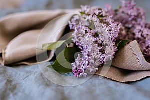 Close-up of purple lilac flowers branch in bloom on blue linen sheet with neutral linen towel, eco lifestyle concept, still life,