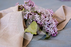 Close-up of purple lilac flowers branch in bloom on blue linen sheet with neutral linen towel, eco lifestyle concept, still life,