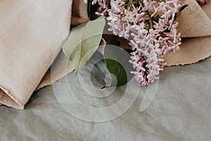 Close-up of purple lilac flowers branch in bloom on blue linen sheet with neutral linen towel, eco lifestyle concept, still life,