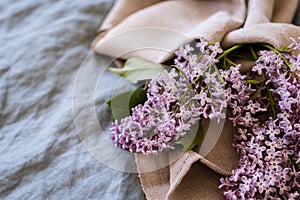 Close-up of purple lilac flowers branch in bloom on blue linen sheet with neutral linen towel, eco lifestyle concept, still life,