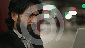 Close-up puzzled serious Indian man looking at laptop screen in underground parking focused worried young arabian