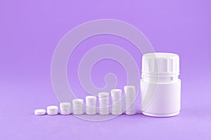 Close up pyramid concept of white pills and bottle on purple background with copy space. Focus on foreground, soft bokeh. Pharmacy