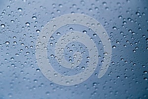 Close up of rain drops on window with blue gray background of dark sky