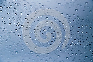 Close up of rain drops on window with blue gray background of dark sky