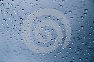 Close up of rain drops on window with blue gray background of dark sky