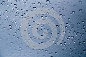 Close up of rain drops on the windshield, front window of a car on a blue gray background of dark sky.