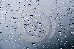 Close up of rain drops on the windshield, front window of a car on a blue gray background of dark sky