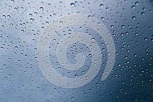 Close up of rain drops on the windshield, front window of a car on a blue gray background of dark sky.