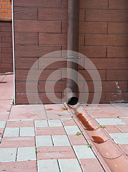 Close up on rain gutter downspout pipe for roof runoff with open water drainage in the pavement. photo