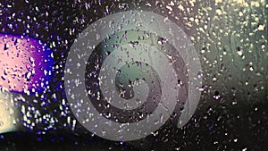 Close up of rain water drops on car window glass with blurred traffic lights background at night.