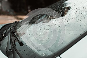 Close-up of raindrops on the windshield of a car in cloudy weather after rain outdoors. Side view, selective focus