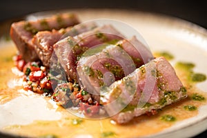 Close-up of rare tuna steak slices with vegetable and sauce on a plate.