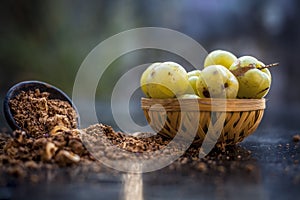 Close up of raw amla or Phyllanthus emblica or Indian gooseberry in a fruit basket with its dried seed powder in a clay bowl used