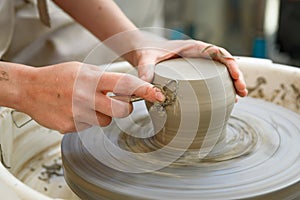 close up of raw ceramic running on the lathe or potter's wheel, with hands with tool refining fine details of vase