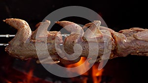 Close-up of raw marinated quails on the skewer rotated above the open fire