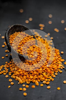 Close up of Raw Masur dal or masoor lentils or pink lentils in a black colored clay bowl on wooden surface