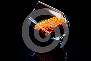 Close up of Raw Masur dal or masoor lentils or pink lentils in a black colored clay bowl on black in wineglass glass jar bucket