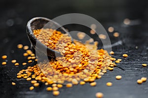 Close up of Raw Masur dal or masoor lentils or pink lentils in a black colored clay bowl on wooden surface.